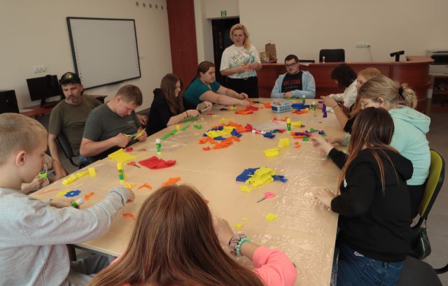 młodzież siedzi przy stołach ustawionych w kwadrat, na stołach kolorowa bibuła