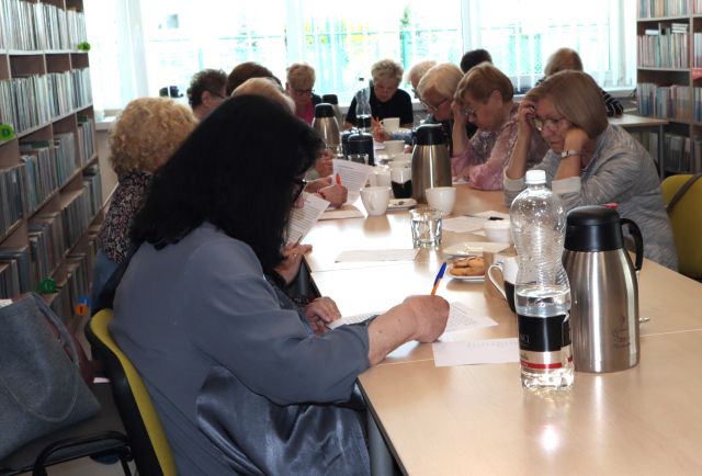 seniorki siedzą przy połączonych stołach, na stołach kartki i filiżanki