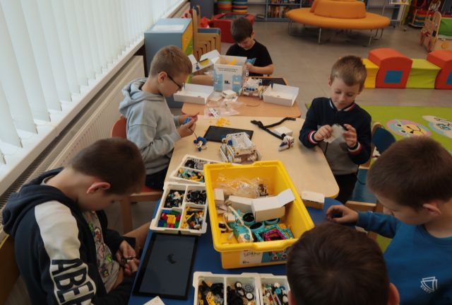 na stołach rozłożone klocki LEGO, przy stolikach siedzią dzieci i składają klocki