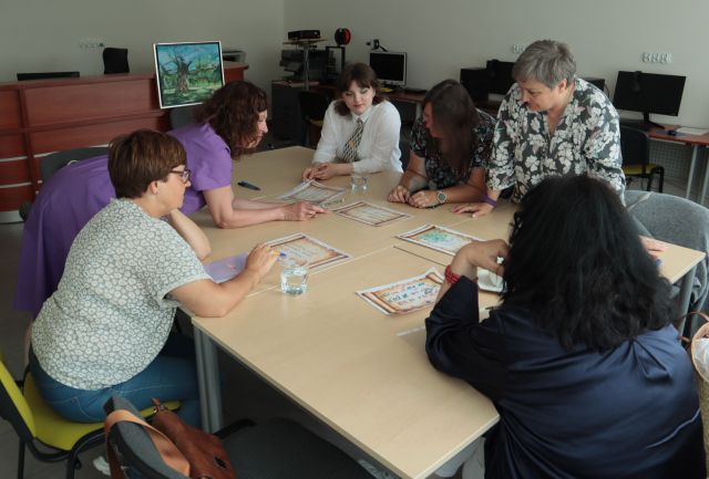 uczestniczki warsztató siedzą przy połączonych stołach, na stołąch kartki, długopisy i filiżanki
