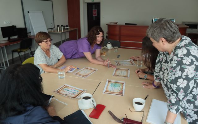 uczestniczki warsztató siedzą przy połączonych stołach, na stołąch kartki, długopisy i filiżanki