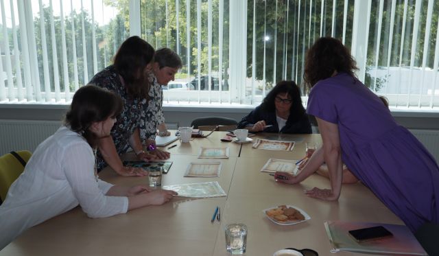 uczestniczki warsztató siedzą przy połączonych stołach, na stołąch kartki, długopisy i filiżanki