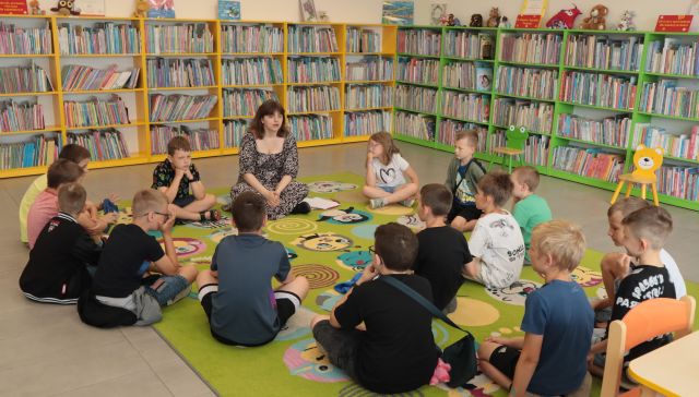 dzieci z bibliotekarką siedzą na kolorowym dywanie
