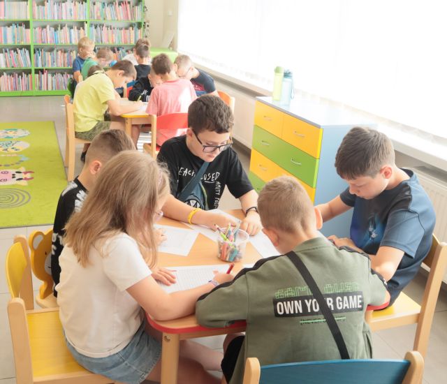 chłopcy siedzą przy stolikach i rysują na kartkach