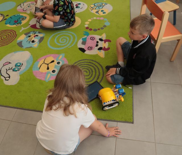 dziewczynka i chłopiec siedzą na dywanie, pomiędzy nimi pojazd z klocków Lego