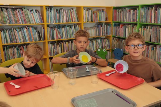3 chłopców prezentuje slimy w miseczkach, w tle regały z książkami