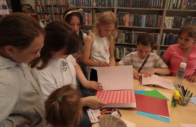 bibliotekarka pokazuje zgromadzonym wokół niej dzieciom książkę z nową okładką