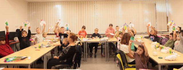 dzieci siedzą przy stołach i robią rakiety z kartek i rolek po papierze toaletowym