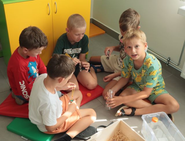 dzieci siedzą na podłodze, przed nimi eduskrzynki z różnymi materiałami