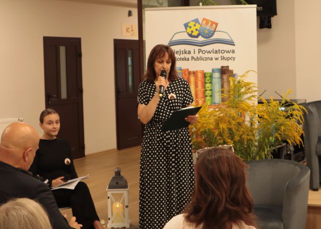 przed publicznością stoi dyrektorka biblioteki z mikrofonem