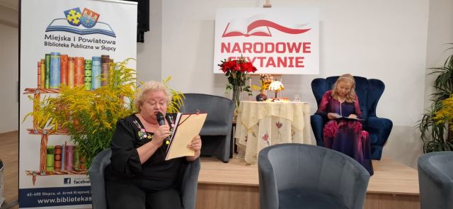 kobieta czyta do mikrofonu, na scenie siedzi w fotelu aktorka