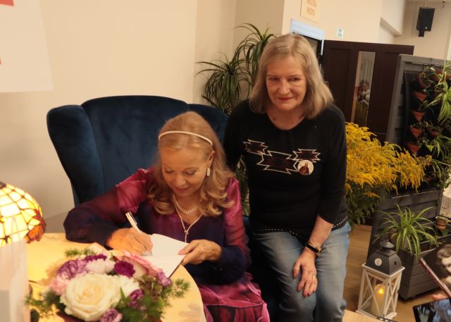 aktorka podpisuje książkę, na oparciu fotela siedzi kobieta