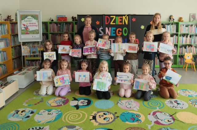 przedszkolaki pozują do zdjęcia z wykonanymi przez siebie rysunkami