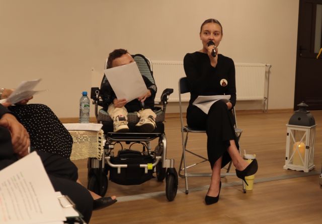 dziewczyna z mikrofonem siedzi na krześle, z jej lewej strony siedzi chłopiec na wózku inwalidzkim