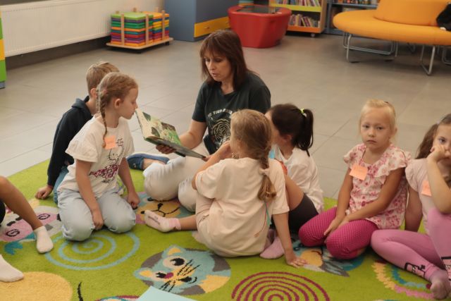 dyrektorka biblioteki czyta dzieciom siedzącym wokół niej na dywanie książkę