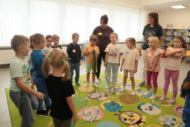 dzieci i nauczycielka stoją w okręgu, chłopiec trzyma w dłoniach maskotkę ryby