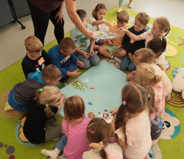 dzieci siedzą wokół dużej niebieskiej kartki