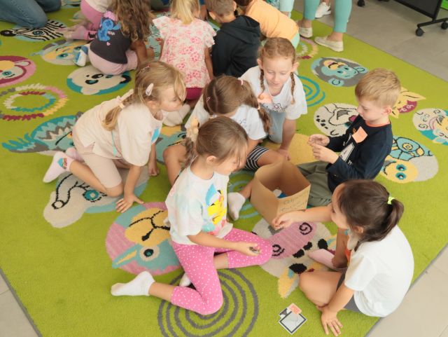 dzieci siedzą wokół kosza na odpady zrobionego z kartonu