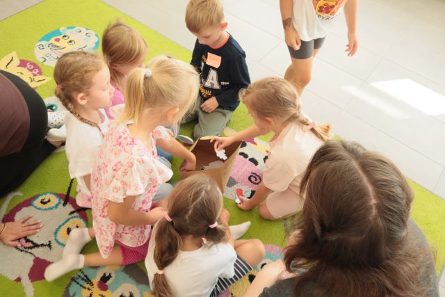 dzieci siedzą wokół kosza na odpady zrobionego z kartonu