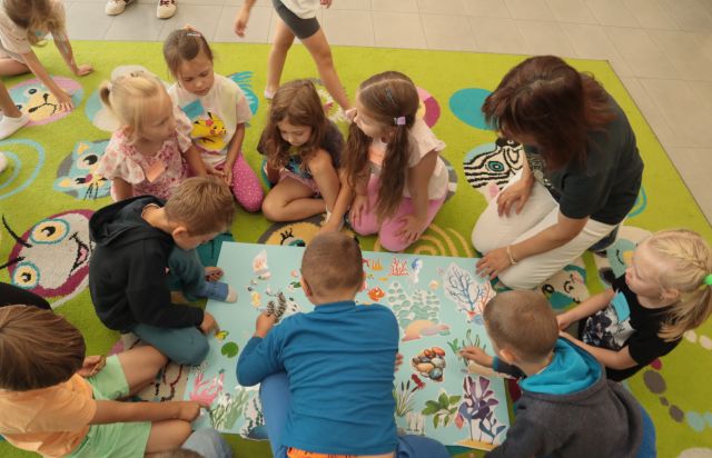 dzieci siedzą wokół dużej niebieskiej kartki, układaja na niej rybki i roślinki i inne zwierzęta wodne