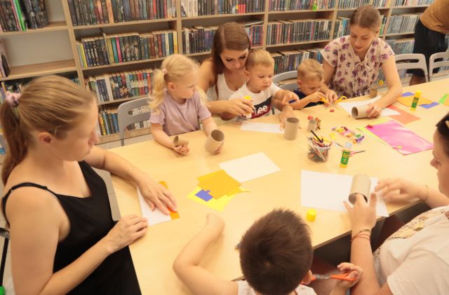 dzieci z rodzicami oblepiają rolki po papierze toaletowym, w tle regały z książkami