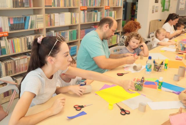 dzieci z rodzicami oblepiają rolki po papierze toaletowym, w tle regały z książkami