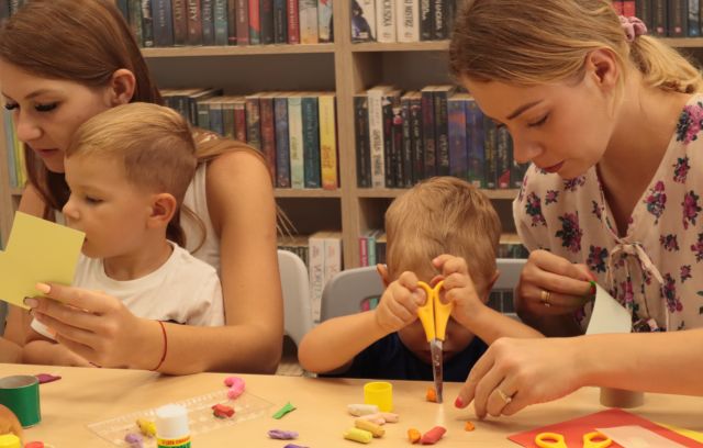 dzieci z rodzicami oblepiają rolki po papierze toaletowym, w tle regały z książkami