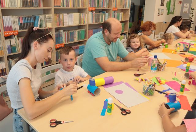 dzieci z rodzicami oblepiają rolki po papierze toaletowym, w tle regały z książkami