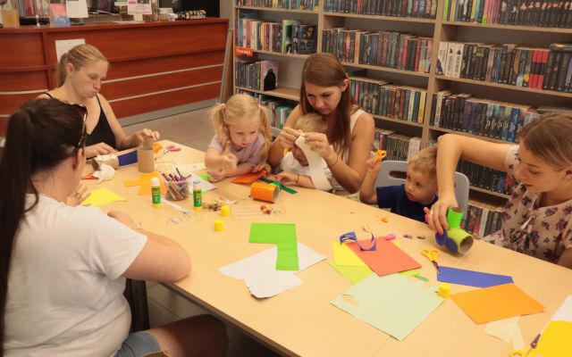 dzieci z rodzicami oblepiają rolki po papierze toaletowym, w tle regały z książkami
