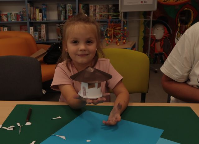 dziewczynka prezentuje na dłoni zrobiony przez siebie z kartek domek smerfów