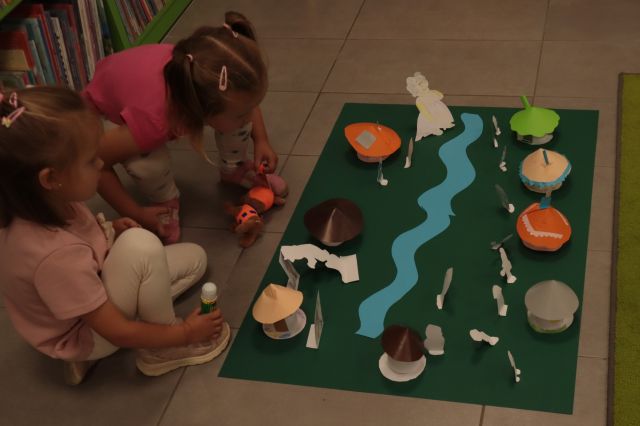 makieta przedstawiająca wioskę smerfó, przed nią siedzą dwie dziewczynki