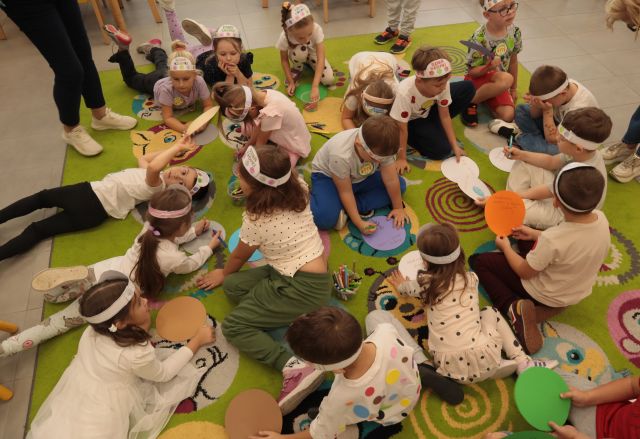 przedszkolaki siedzą na kolorowym dywanie i rysują na kolorowych kartkach w kształcie kółek