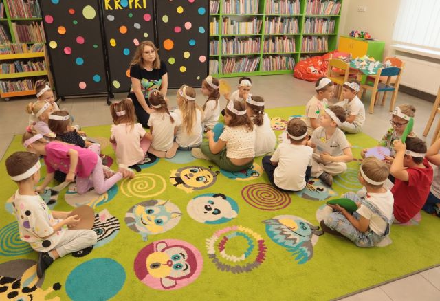 przedszkolaki siedzą na kolorowym dywanie przed bibliotekarką