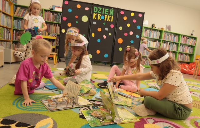 przedszkolaki siedzą i leżą na kolorowym dywanie, przeglądają książki