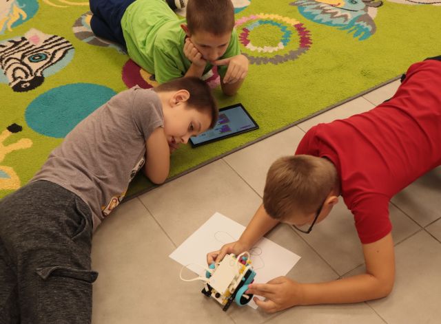 dwaj chłopcy leżą na dywanie i przyglądają się chłopcu z pojazdem zbudowanym z klocków Lego Spike Prime