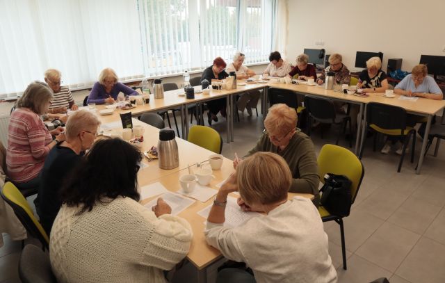 Seniorki siedzą przy stołach i notują na kartkach