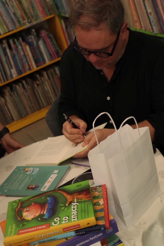 autor przy stoliku podpisuje książkę