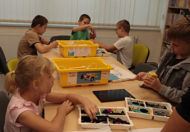 chłopcy i dziewczynka układają klocki Lego