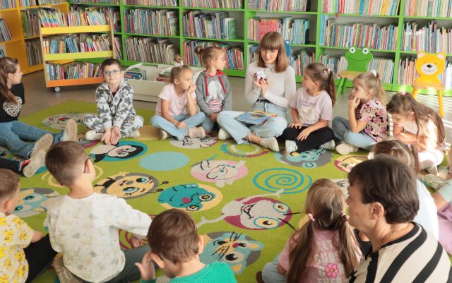 przedszkolaki i bibliotekarka siedzą na kolorowym dywanie