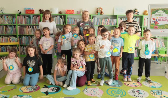 dzieci pozują do zdjęcia z przedszkolanką i nauczycielkami, w tle regały z książkami