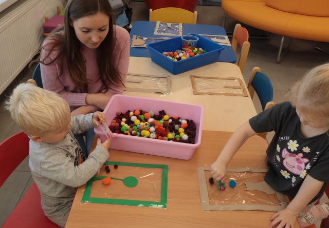 dzieci z mamami układają kolorowe kuleczki w plastikowym pojemniku
