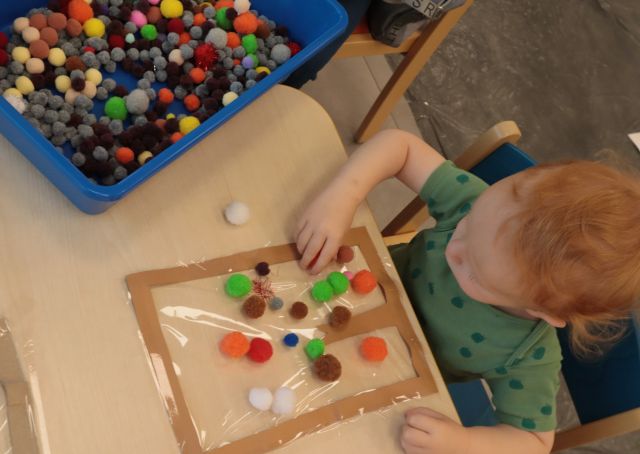 chłopiec układa kolorowe kuleczki na kartce