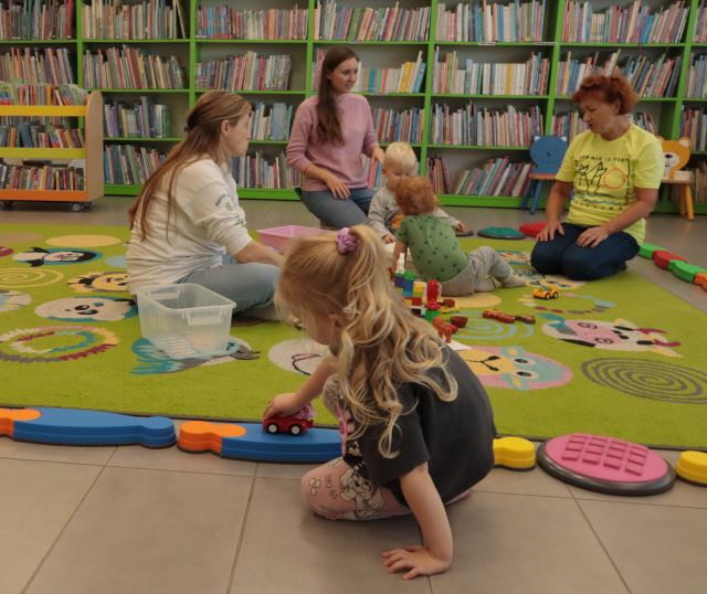 dzieci z mamami siedzą na kolorowym dywanie