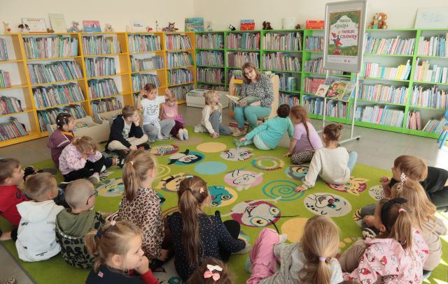 dzieci i bibliotekarka siedzą w okręgu na kolorowym dywanie
