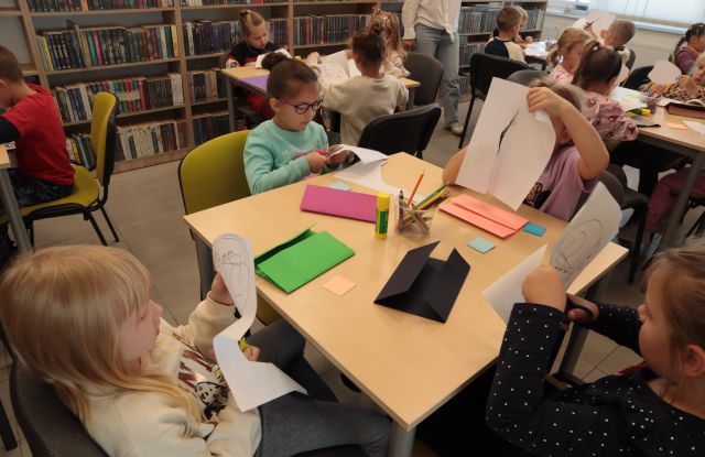 dzieci siedzą przy stolikach i wycinanją z kartek