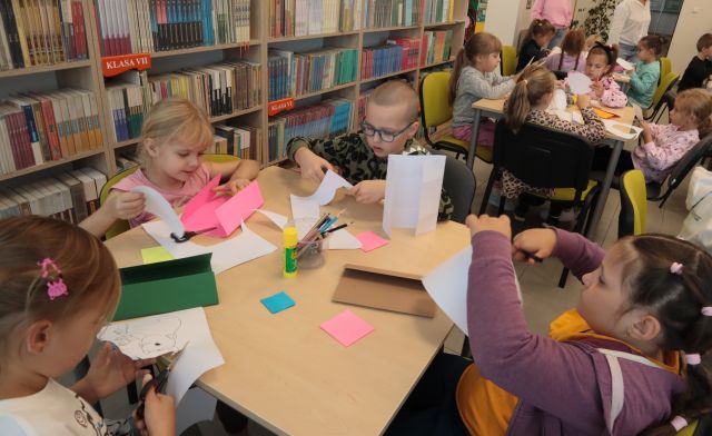 dzieci siedzą przy stolikach i wycinanją z kartek