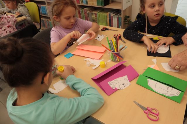 dzieci siedzą przy stolikach i wycinanją z kartek
