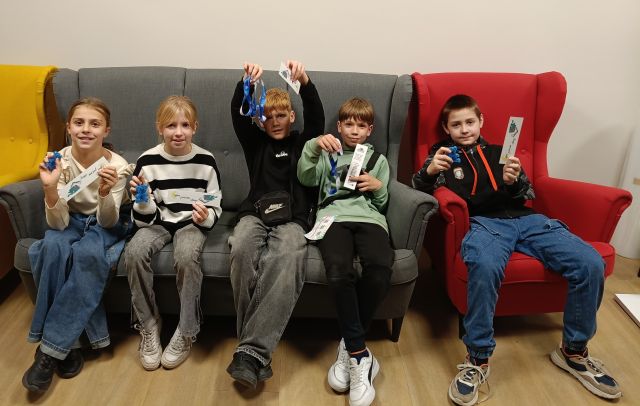 5 dzieci siedzi na sofie i pozuje do zdjęcia ze swoimi nagrodami
