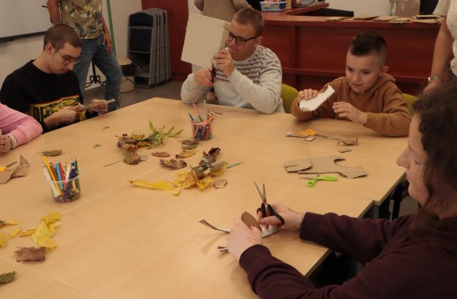 młodzież siedzi przy połączonych stołach i wycina z kartonów