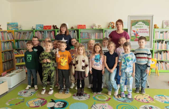 przedszkolaki, bibliotekarka i nauczycielka pozują do zdjęcia, w tle regały z książkami